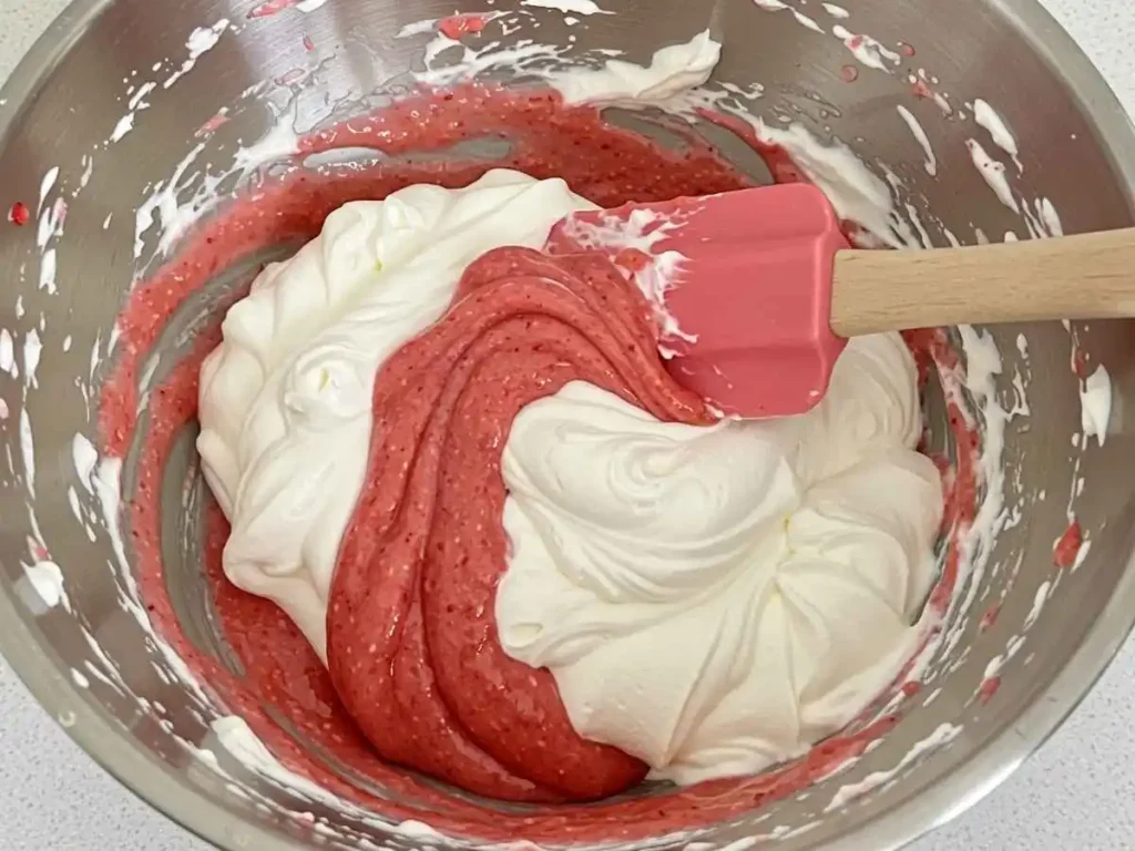 Integrando puré de fresa y nata montada con espátula mediante movimientos envolventes suaves.
