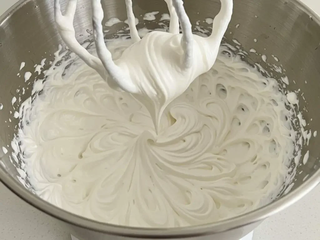 Nata montada (crema de leche batida) a punto de picos suaves en un bol frío.