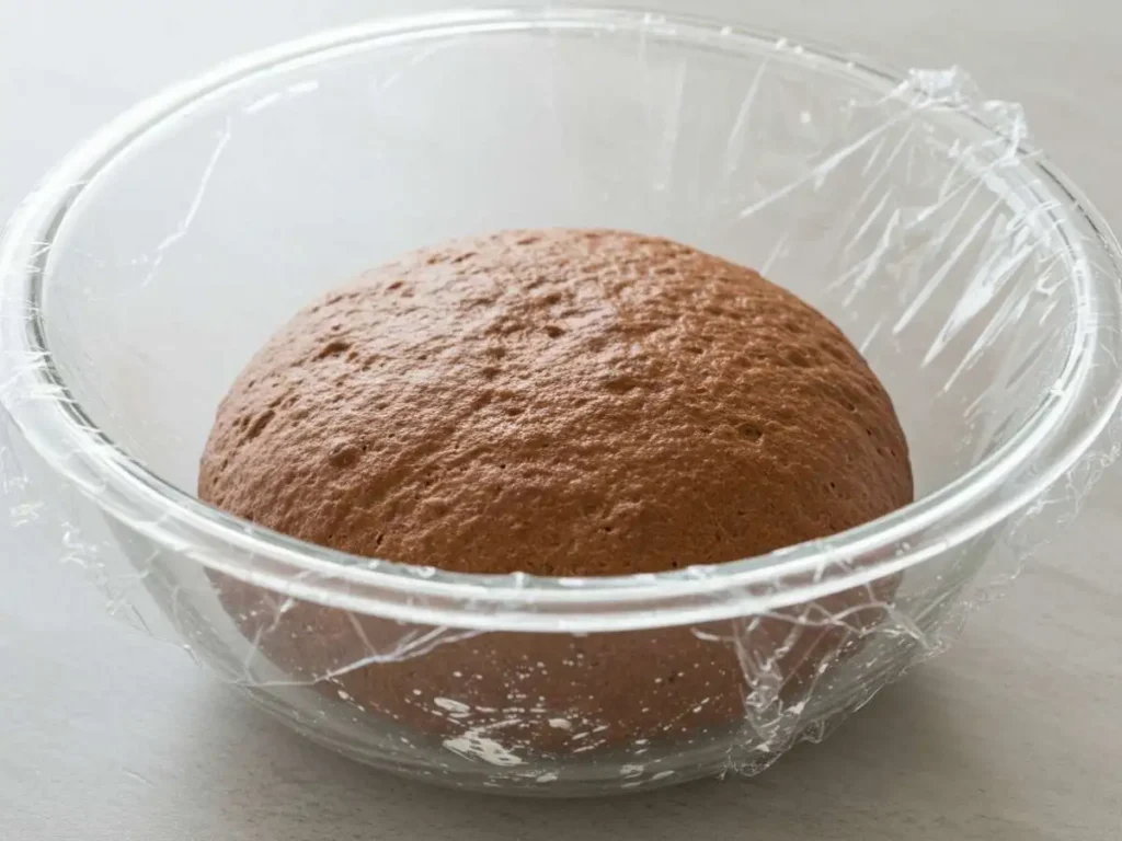 Masa de pan de chocolate que ha duplicado su tamaño en un bowl de cristal después de la primera fermentación.